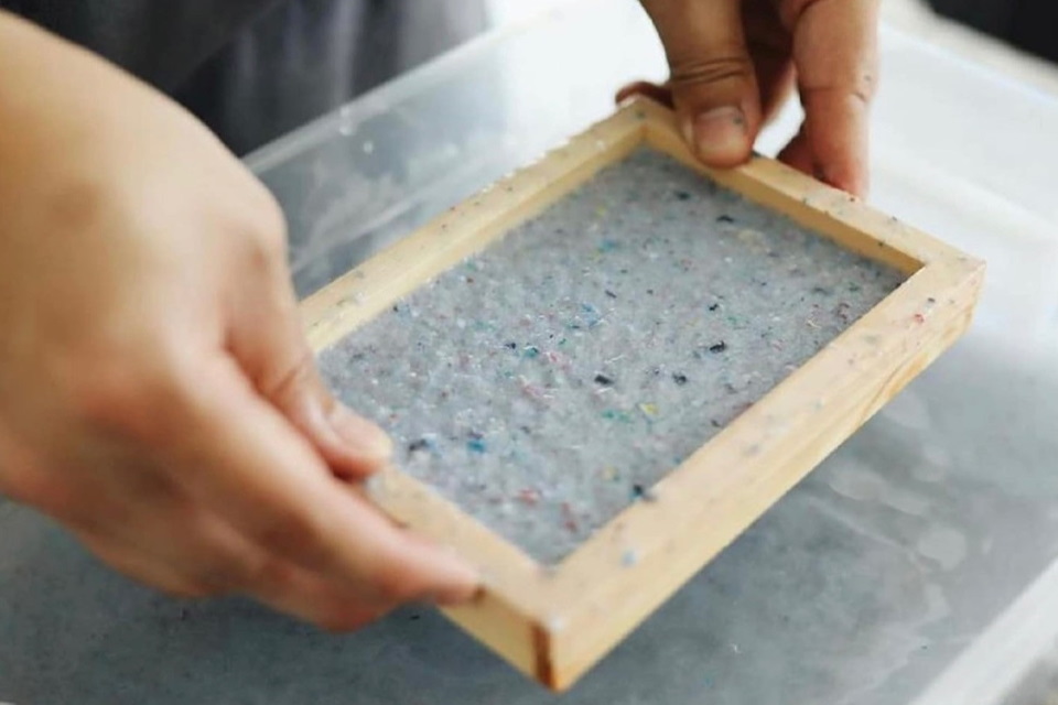 hands holding a wooden frame with pulp inside it for making paper