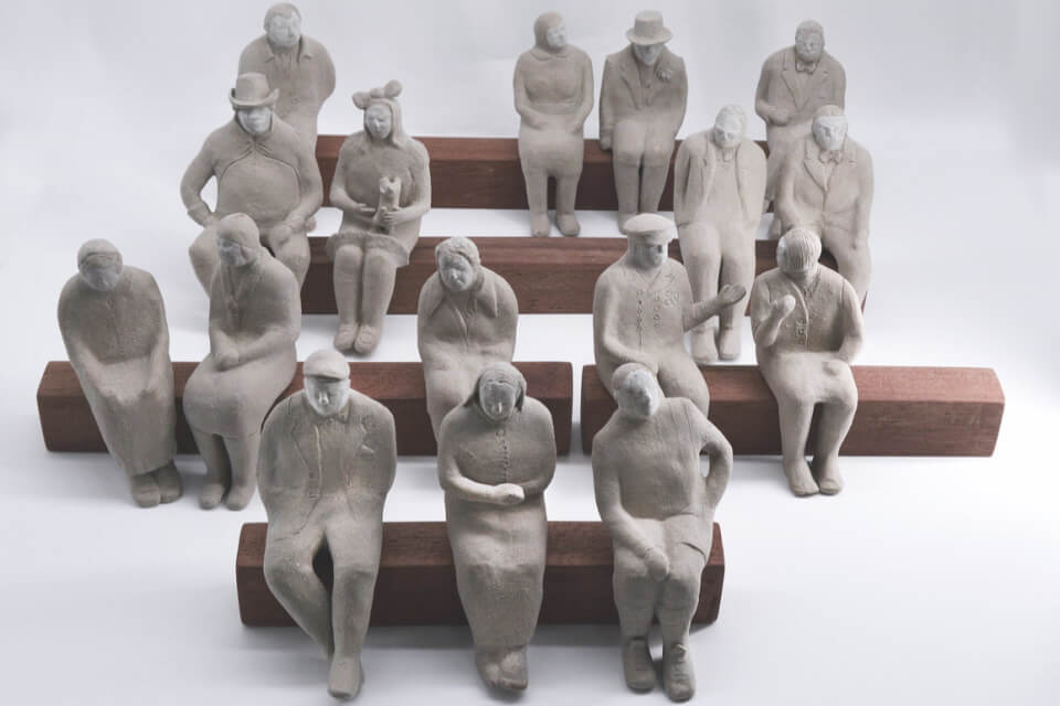 a series of clay figures sitting on four rows of wooden benches