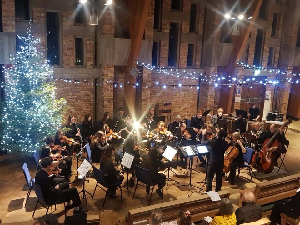 orchestra performing in Chapel under fairy lights with a lit Christmas tree