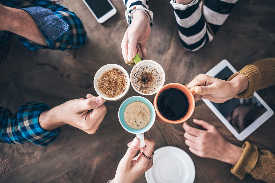 Overhead photograph of four people around a table holding cups of coffee.