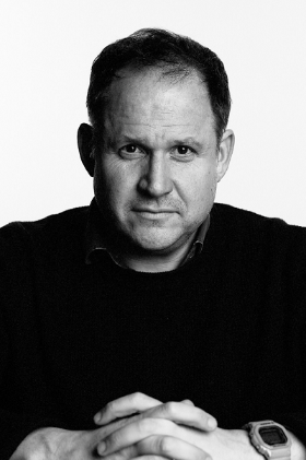 Black and white image of Henry Dimbleby looking at the camera, wearing a dark suit