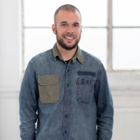 Man smiling wearing denim shirt with window pane in background white light shining through