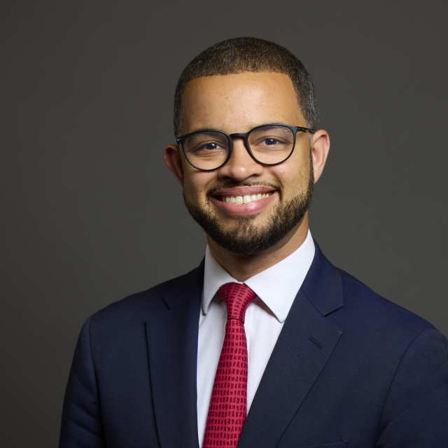 Photograph of Adam Jogee, MP for Newcastle-under-Lyme, wearing a navy suit, white shirt and red tie.